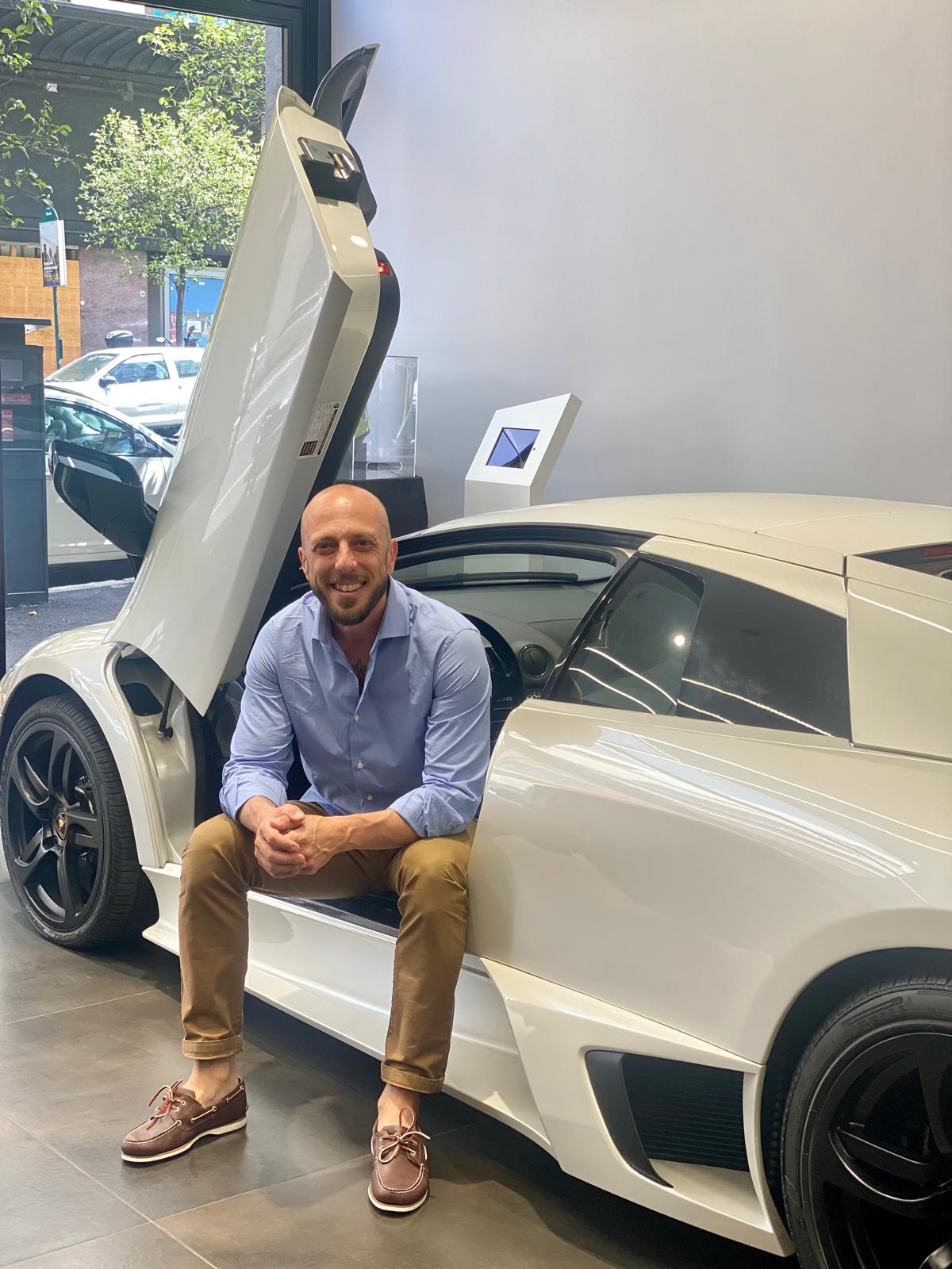 Federico Cappa seduto sulla Lamborghini Murciélago bianca porte ad ali di gabbiano showroom Milano